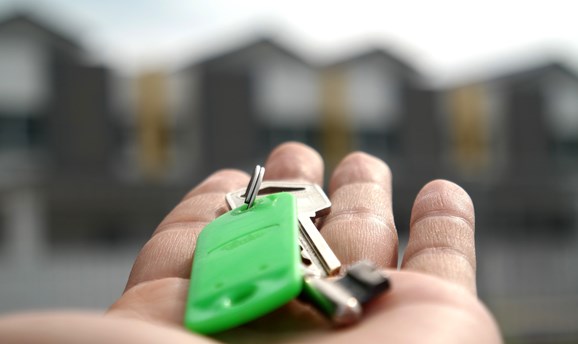 a hand holding keys in front of a row of houses 