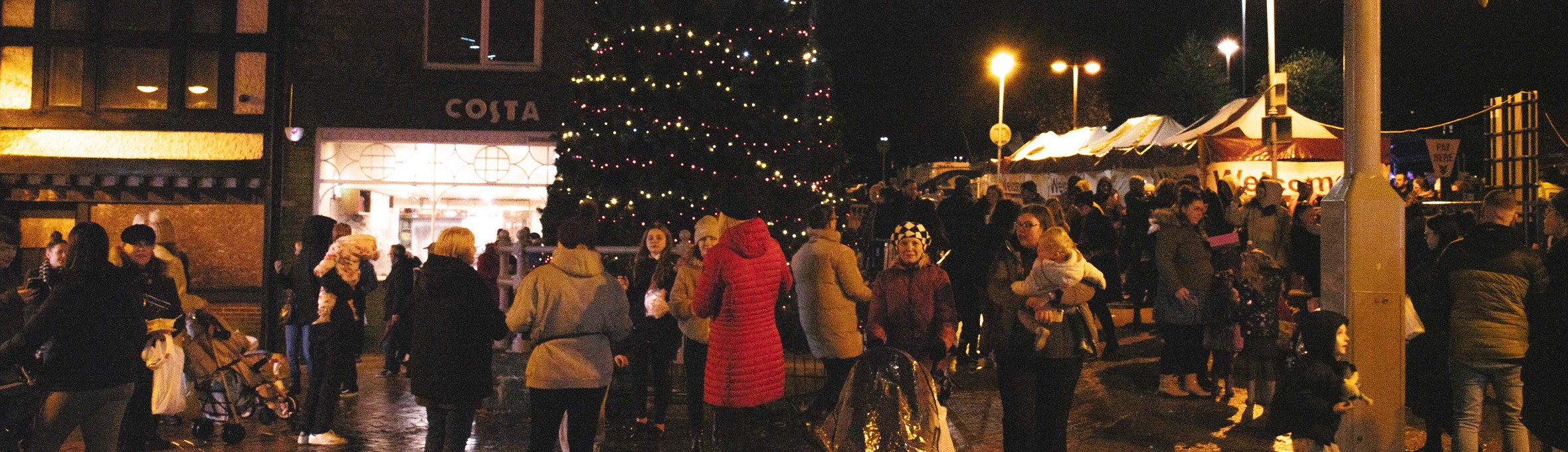 Crowds of people in front of a big Christmas tree with market stalls in the background