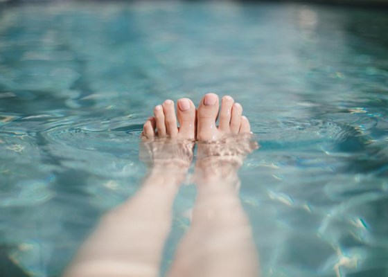 Baby pink painted toes peeking out of a swimming pool