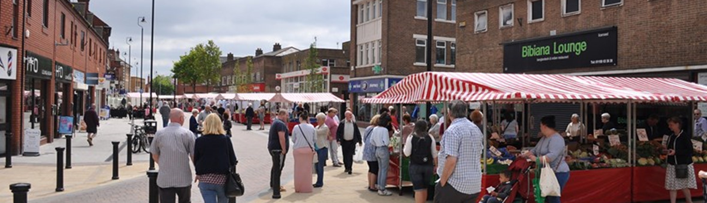 Hucknall outdoor market with stalls along pedestrianised road and people shopping