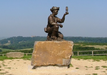 Statue of a miner holding up a Davey lamp, rock plinth, with open view of countryside behind