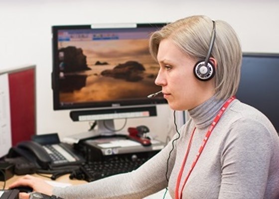 Female Lifeline operator sat in profile at computer with phone headset on