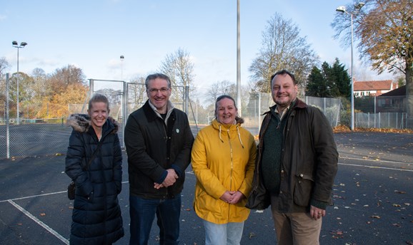 two women and two men smile at the camera, they are stood on a tennis court on Sutton Lawn