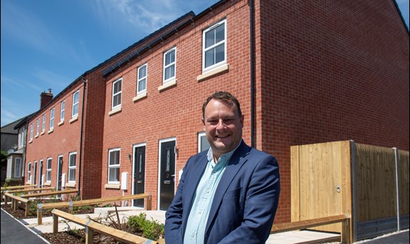 Cllr Jason Zadrozny stands, smiling in a jacket, in front of the five new homes in Sutton