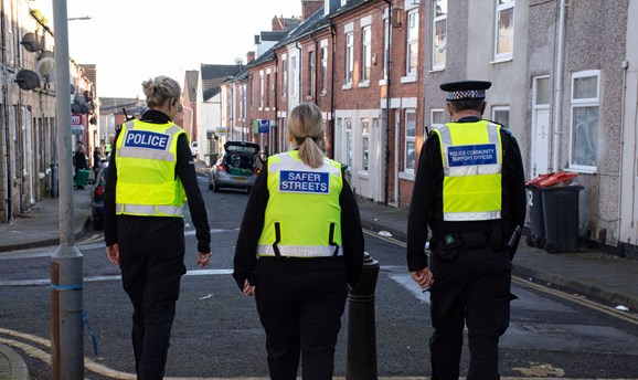 a police woman, a cpo and pcso wear high vis vests whilst walking through a street 
