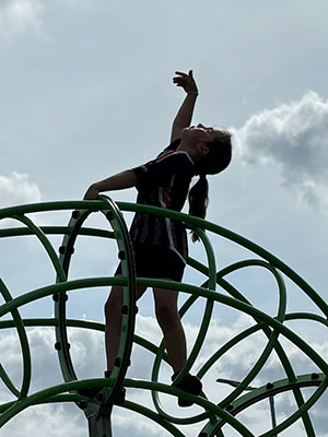 Reach For The Skies by Tracy Hancock - a child climbing on a climbing frame, with one arm reaching