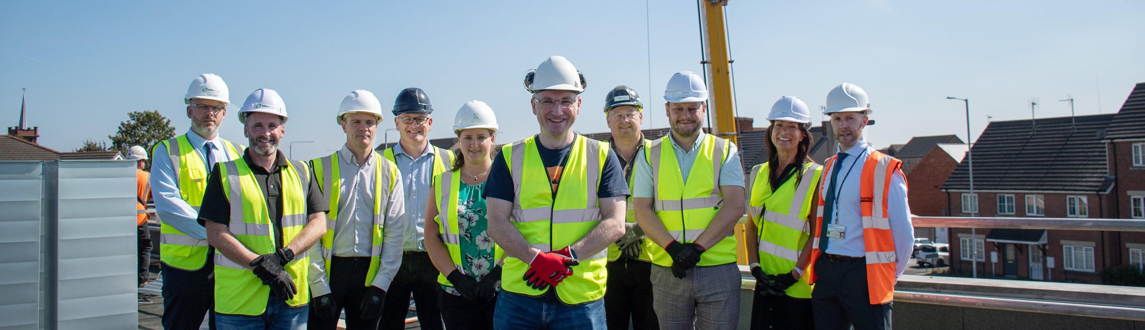 a group of people in high vis vests and hard hats stood on a roof with a crane in the background