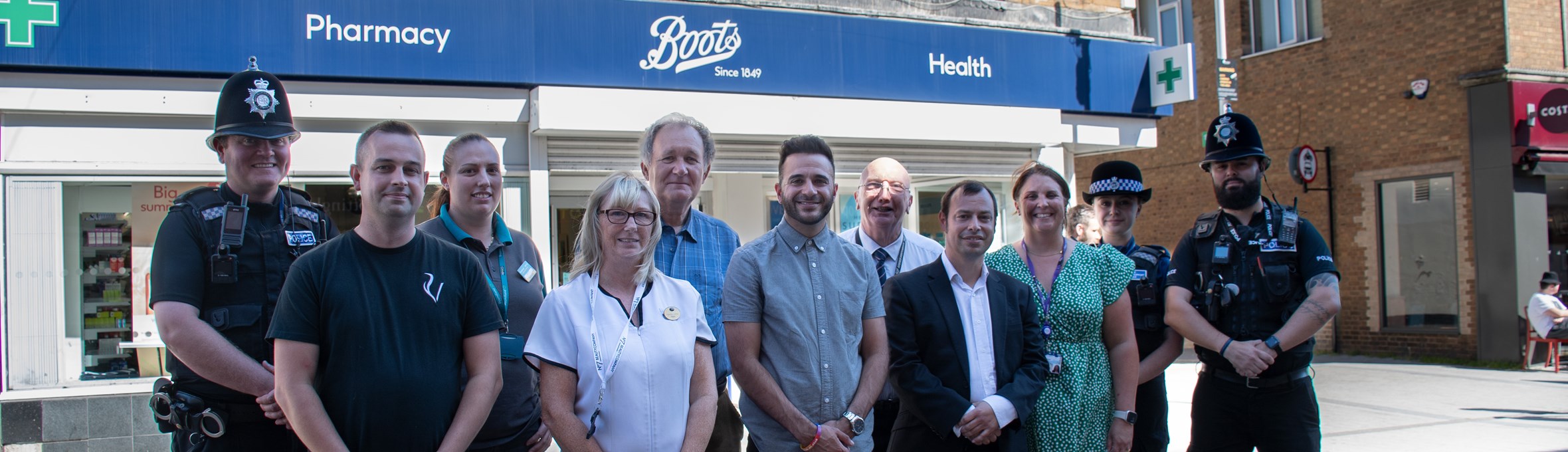 a group of people are stood on Hucknall High Street in front of the shop Boots 